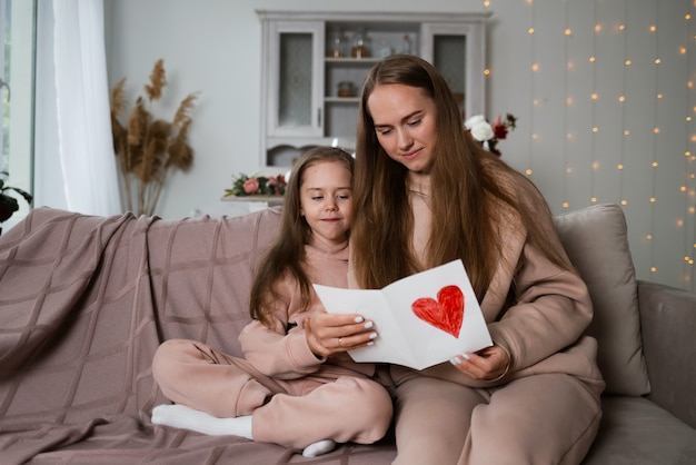 Een mooie moeder en dochter zitten op de bank en kijken naar een ansichtkaart met een hart