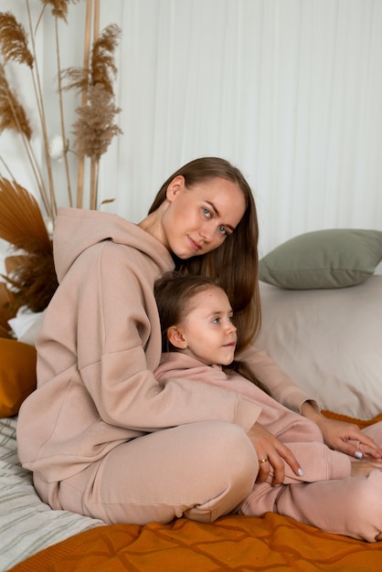 Een mooie moeder en een dochtertje in identieke pakken zitten op het bed