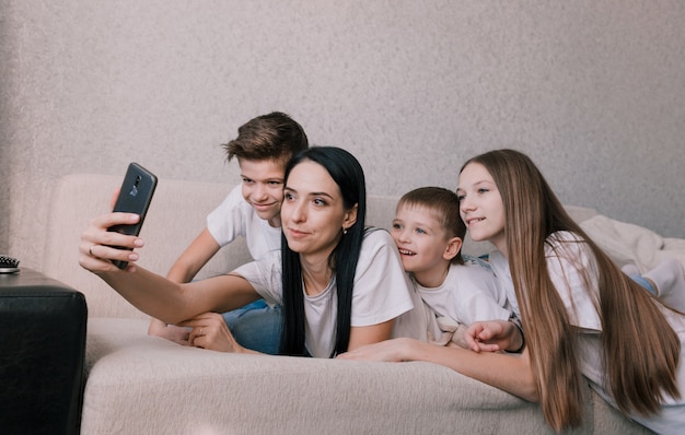 Een mooie moeder met haar kinderen neemt een selfie op haar telefoon terwijl ze op de bank ligt en gelukkig vriendelijk gezin