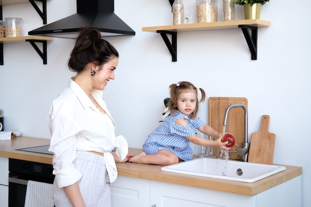 Een mooie moeder met haar twee jaar oude dochter wast fruit in de gootsteen