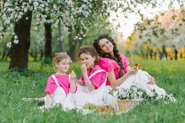 Een mooie moeder, twee dochters in lichte kleren, picknicken in de lentetuin Outdoor