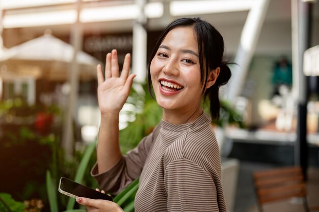 Een mooie positieve Aziatische vrouw staat buiten met een smartphone en glimlacht naar de camera