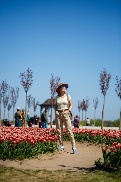 Een mooie slanke vrouw met een hoed staat in een bloeiend tulpenveld Lentetijd