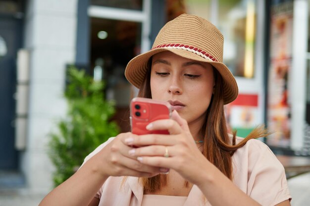 Foto een mooie spaanse vrouw met een hoed die op een zonnige dag in een café zit met haar mobiele telefoon