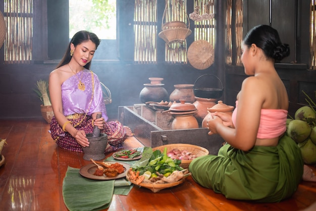 Een mooie Thaise vrouw en ze draagt traditionele Thaise kostuums, zowel meesters als bedienden. Ze zitten en koken in de keuken. Concept van het leven in het verleden van de Ayutthaya-mensen