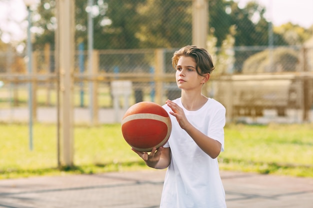 Een mooie tiener in een wit t-shirt staat op het basketbalveld en houdt een basketbal vast