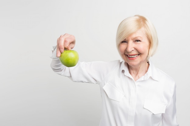 Een mooie volwassen vrouw die een groene appel in de rechterhand houdt. Ze eet graag fruit. Dit is haar keuze.