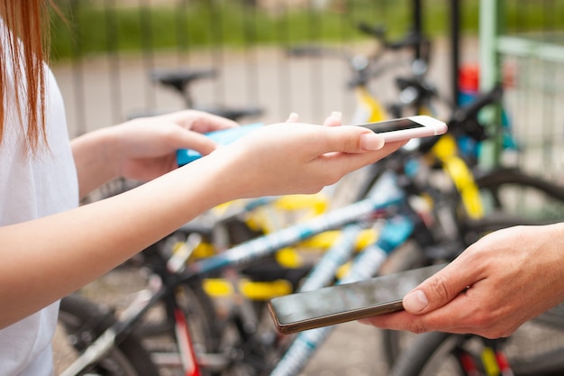 Een mooie vrouw betaalt een fietshuur met een telefoon en een bankkaart. mobiele betaling. Huur een fiets voor een dag. Technologie, internet, smartphone close-up