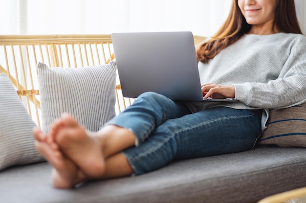 Een mooie vrouw die een laptop gebruikt en eraan werkt terwijl ze thuis op een bank zit