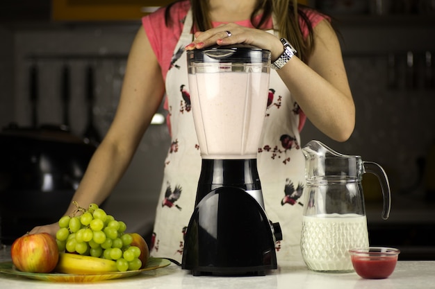 Een mooie vrouw die een melkcocktail met fruit in de keuken voorbereidt