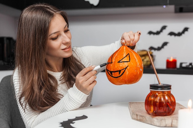 Een mooie vrouw die een pompoen schildert op Halloween, zittend aan de keukentafel