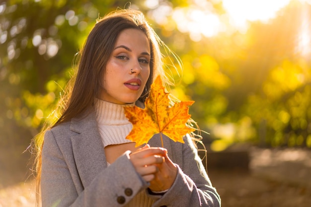 Een mooie vrouw die geniet van de herfst in een park bij zonsondergang met een blad van de boom