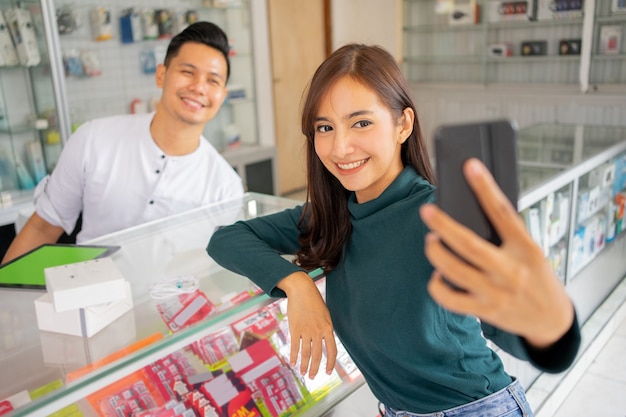 Een mooie vrouw glimlacht terwijl ze een selfie maakt met een mobiele telefoon terwijl ze zit met een man die in de buurt zit...