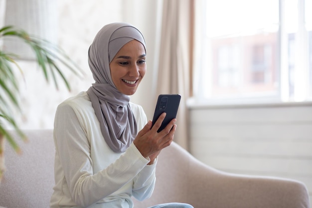 Een mooie vrouw in een hijab gebruikt de telefoon van dichtbij een moslimvrouw zit op de bank