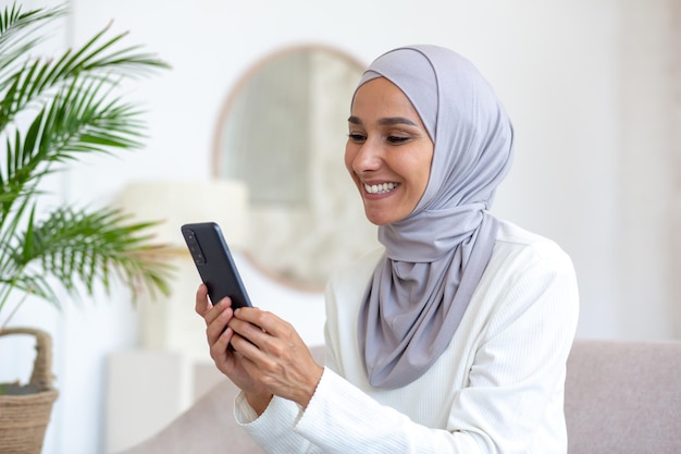 Een mooie vrouw in een hijab gebruikt de telefoon van dichtbij een moslimvrouw zit op de bank