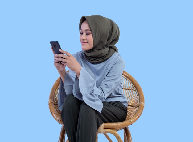 Een mooie vrouw in een hijab zit op een stoel en kijkt naar het telefoonscherm