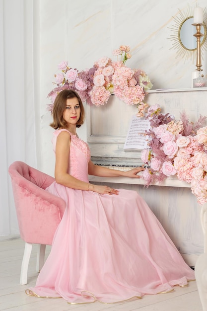 Een mooie vrouw in een lange roze jurk in een hal met bloemen het meisje is mooi lente fotosessie