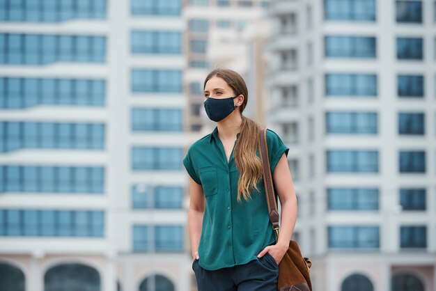 Een mooie vrouw in een medisch gezichtsmasker steekt tijdens het lopen handen in broekzakken