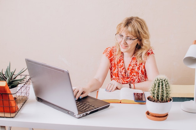 Een mooie vrouw in een rode blouse zit op kantoor en werkt op een laptop