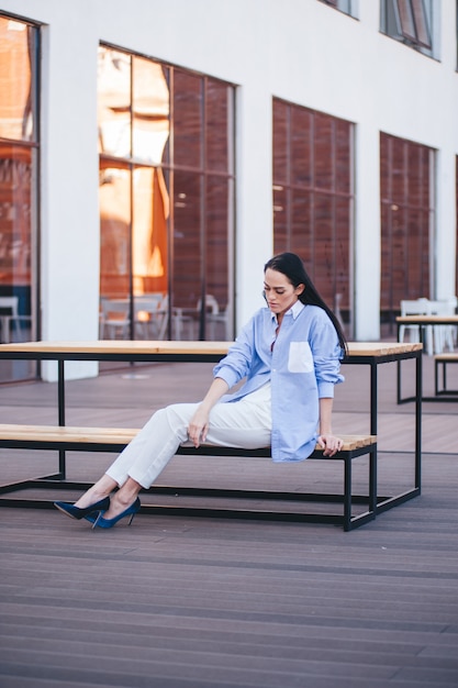 Een mooie vrouw in een shirt en broek zit op een balkon van een bu