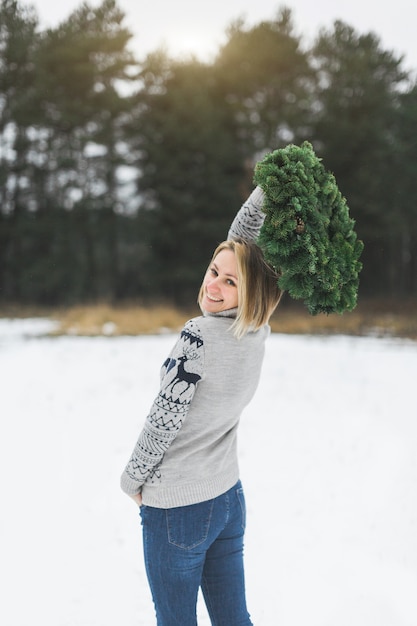 Een mooie vrouw in trui en spijkerbroek houdt een kerstkrans buiten