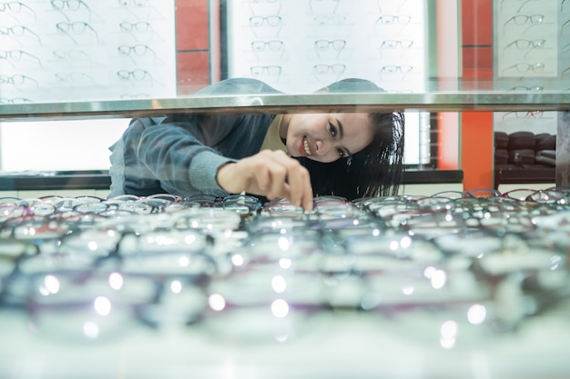 Een mooie vrouw kiest een brilmontuur dat op de vitrine van de oogkliniek staat tegen de brillenvitrine