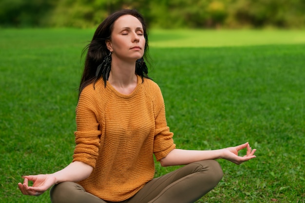 Een mooie vrouw mediteert zittend op het groene gras in het Park