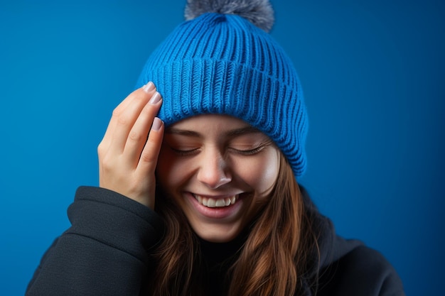 een mooie vrouw met een blauwe gebreide muts lacht op een blauwe achtergrond