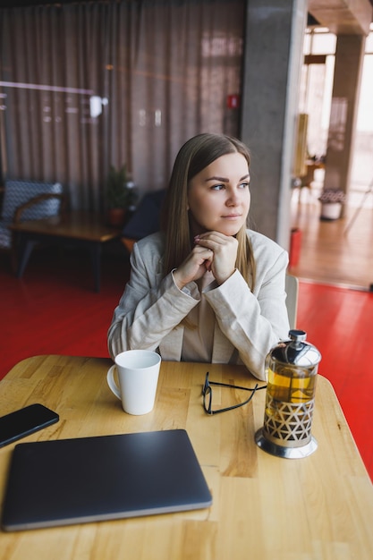 Een mooie vrouw met een Sloveens uiterlijk, een manager in een licht jasje en een bril, een meisje met een glimlach op haar gezicht zit aan een houten tafel in een café Werk op afstand