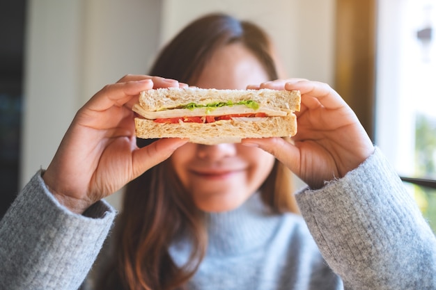 Een mooie vrouw met een smiley die een stuk volkoren boterham vasthoudt, bedekt haar ogen