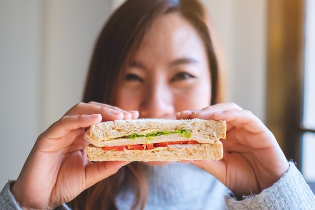 Een mooie vrouw met een smiley die een stuk volkoren broodje vasthoudt, bedekt haar gezicht