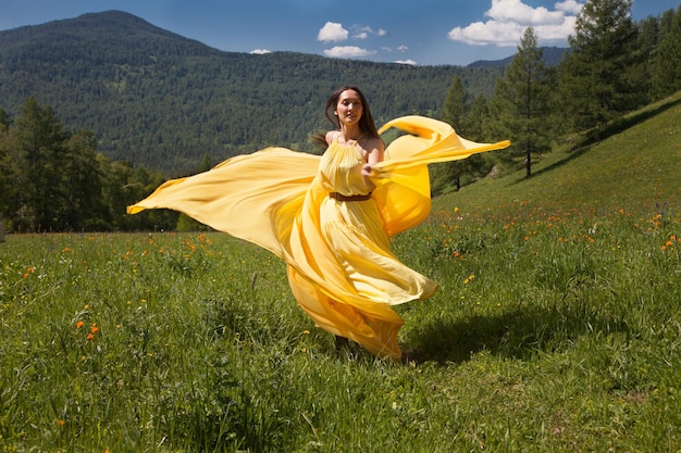 Een mooie vrouw van Aziatische verschijning in een gele jurk loopt in de zomer in Altai.