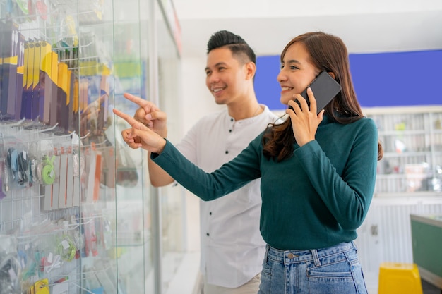 Een mooie vrouw wijst naar een glazen vitrine terwijl ze accessoires voor mobiele telefoons kiest choosing