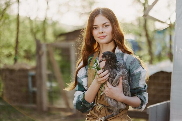 Een mooie vrouwelijke boer zorgt voor de kippen op haar boerderij en houdt een grijze kip lachend vast Het concept van biologisch leven en zorg voor de natuur Hoogwaardige foto