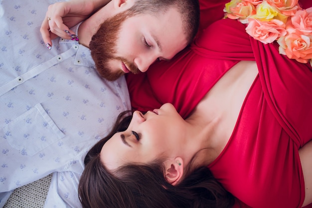 Een mooie zwangere vrouw in zwart ondergoed ligt op een grijze sluier. Het bed is versierd met verse bloemen. Het meisje heeft blond haar, ze glimlacht. Uitzicht van boven.