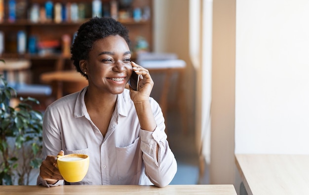 Een mooie zwarte dame die aan het bellen is in een koffieshop.