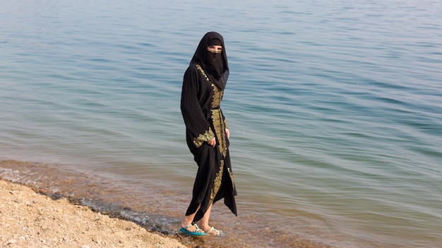 Een moslimvrouw in nationale kleding maakt haar voeten nat in de zee