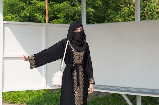 Foto een moslimvrouw in nationale kleding vangt een auto bij een stadshalte met een handgebaar.