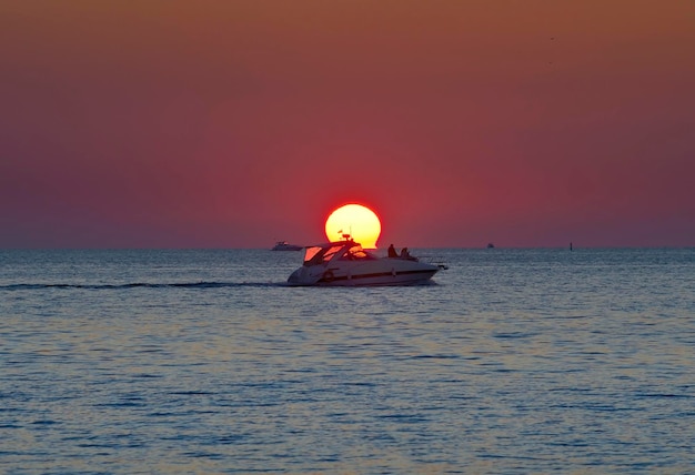 Een motorboot op het water bij de zonneschijf tegen de achtergrond van een robijnrode hemel Sochi, Rusland