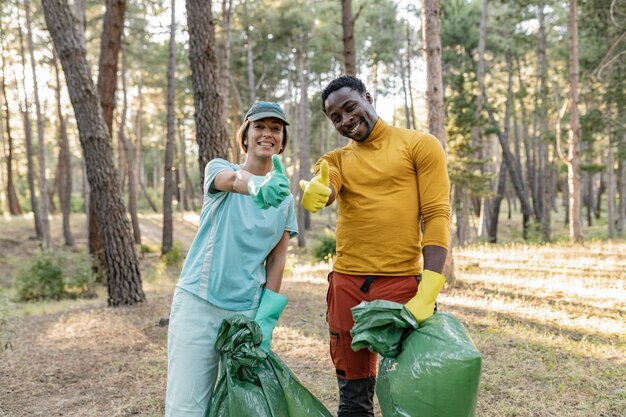 Een multiracial paar vrijwilligers die het park van vuilnis schoonmaken lopen door het bos en dragen plastic zakken Outdoor schoonmaakconcept