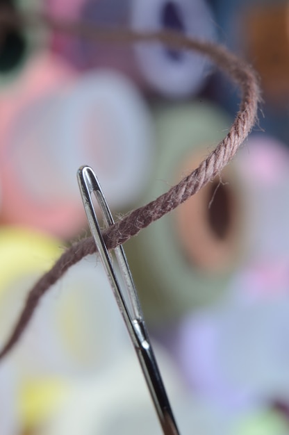 Een naainaald met bruine draad door het oog van de naald. macro.