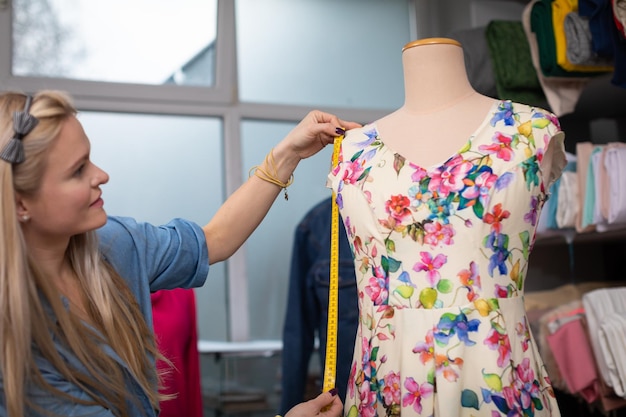 Foto een naaister meet een jurk die aan een mannequin hangt met een centimeter van een kleermaker
