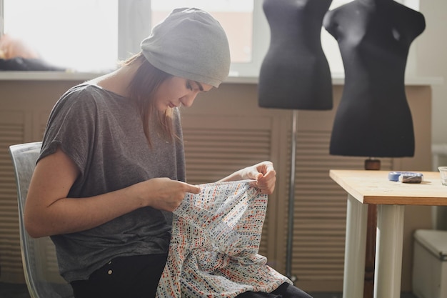 Een naaister naait kleding zittend met een naald in de Studio