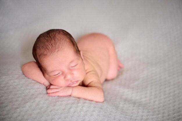 Een naakte pasgeborene slaapt op haar handen bovenop een grijze deken