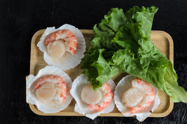 Een natuurlijke rauwe coquille met een garnalenstaart in de schaal met een slablad in een houten kom op een donkere achtergrond