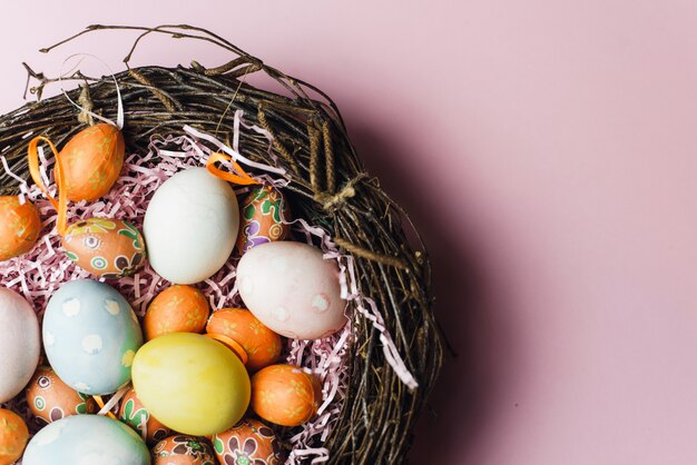 Een nest van takjes en hooi en een roze papiervuller met pastelkleurige paaseieren. Beschilderde en decoratieve eieren voor een lichte paasvakantie. Paaskaart op een roze achtergrond