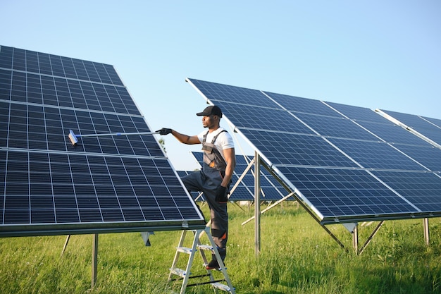 Een netjes Afrikaans-Amerikaanse werknemer maakt zonnepanelen schoon met een speciale bezem.