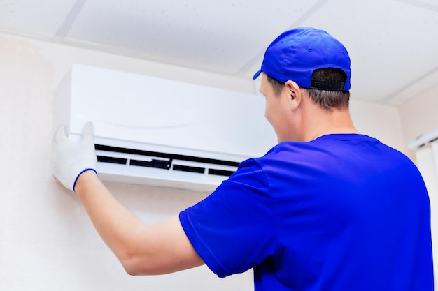 Een nette technicus met een blauwe baseballpet en overall bevestigt de nieuwe airconditioner aan de muur in de kamer