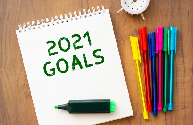 Een notitieboekje met de tekst 2021 GOALS op een bruin houten tafel met gekleurde pennen