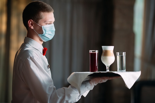 Een ober in europese stijl met een medisch masker serveert latte-koffie.